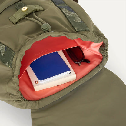 A close up of The Travel Cinch Backpack in Forest showing the interior pockets with a book inside.